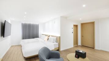 A modern hotel room with a large bed, a grey armchair, a bedside table, and a TV mounted on the wall.