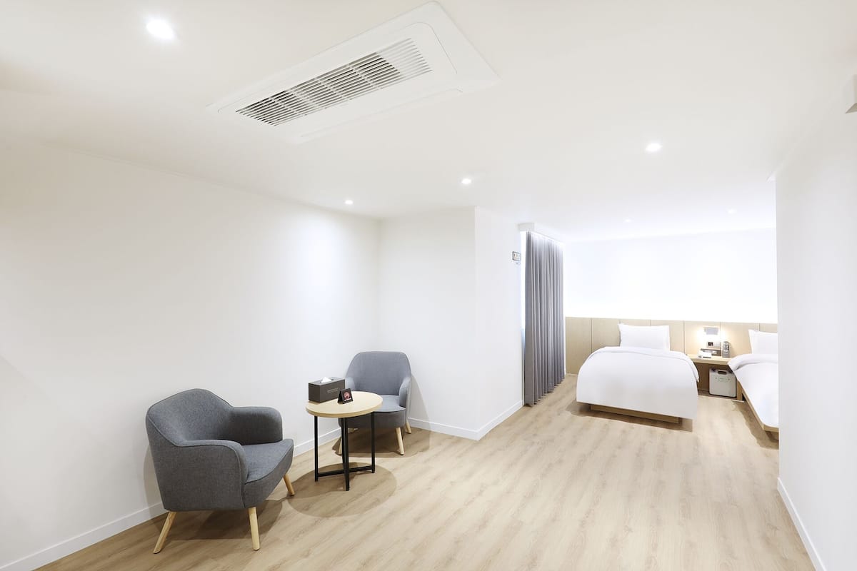 A hotel room with a bed, two chairs, a small table, a nightstand, and a window with curtains.