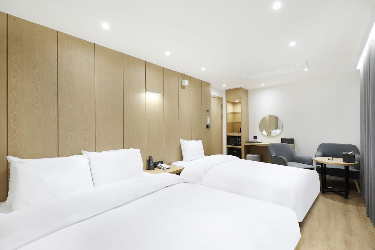 A hotel room with two beds, a desk, a chair, a microwave, and a mirror.