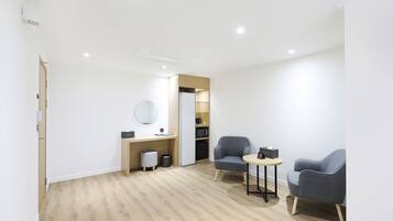A modern, well-lit room with a wooden floor, a desk with a computer, a microwave, and a small seating area with two chairs.