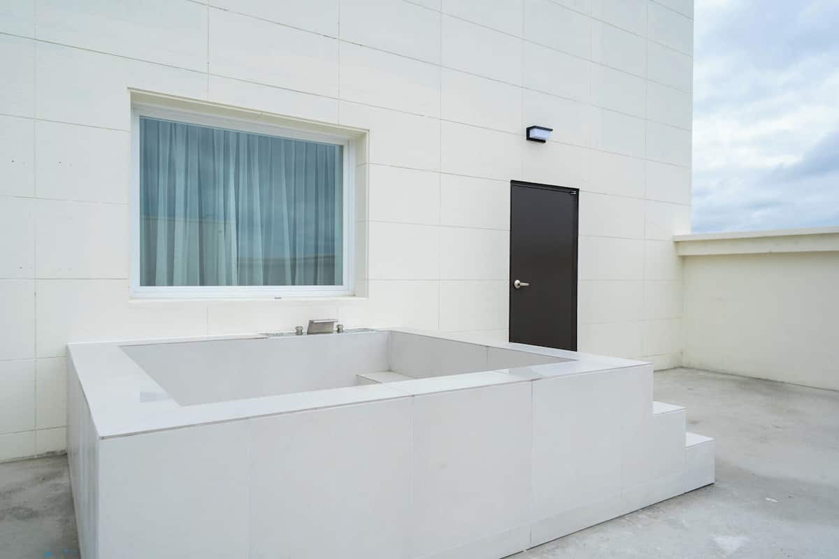 A modern bathroom with a large bathtub, a window with curtains, and a door.