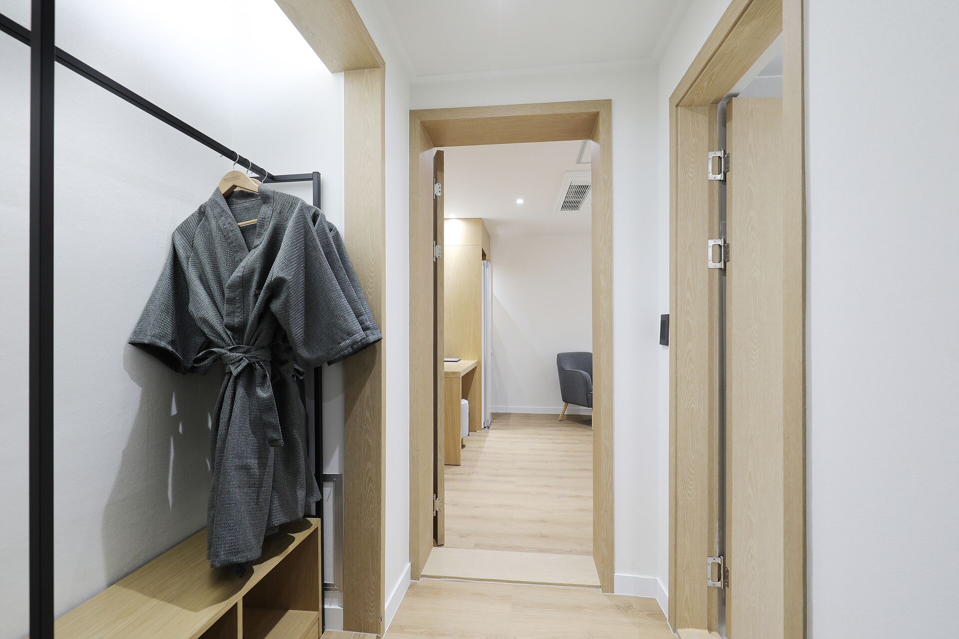 A hallway with a wooden bench, a robe hanging on a rack, and a door with a metal handle.