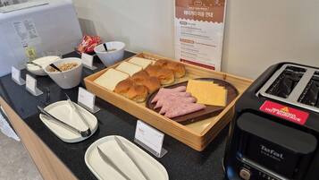 Buffet de l'esmorzar amb pa, pastissos, formatge i pernil. També hi ha bolos de cereals i una torradora.