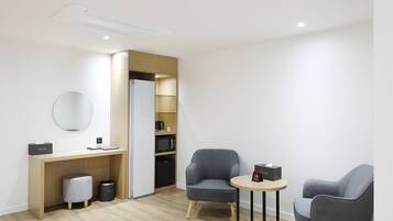 A modern, minimalist room with a wooden desk, two grey armchairs, a round mirror, and built-in shelving.