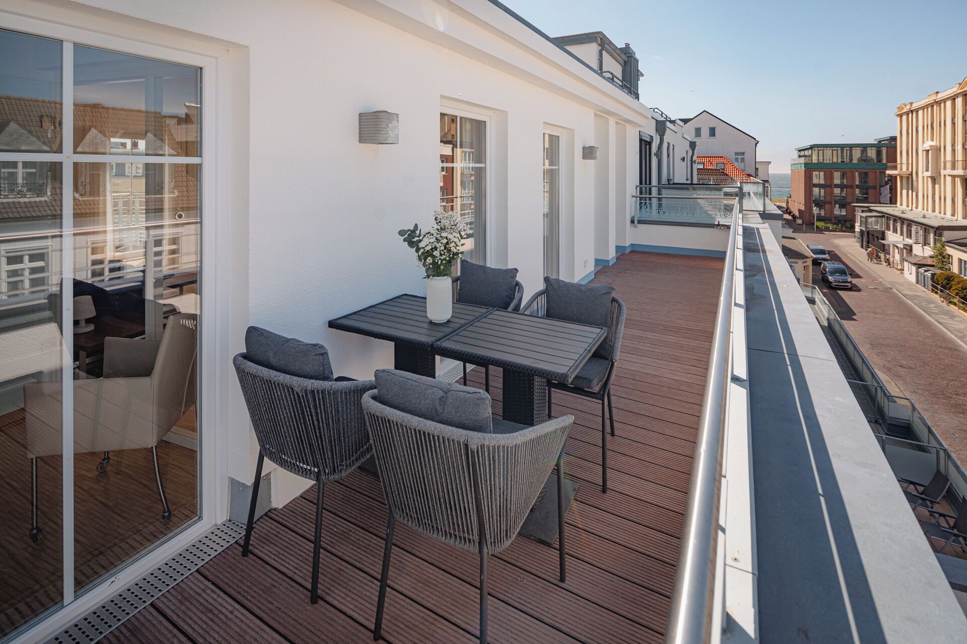 Een balkon met een tafel en stoelen, een bloempot en uitzicht op de straat.