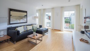 A modern living room with a black sofa, a wooden coffee table, and a painting on the wall.