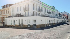 A multi-story building with a white facade, multiple balconies, and a cobblestone street in front.
