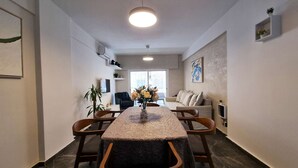 Una sala de estar moderna con un sofá, una mesa de comedor con sillas, un televisor y una planta.