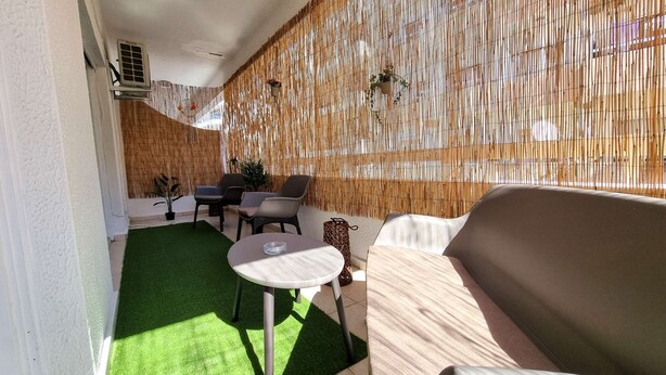 Un patio con césped artificial verde, una mesa redonda, dos sillas, un sofá y un muro de bambú.
