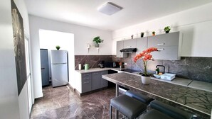 Una cocina moderna con encimera de mármol, horno empotrado y lavabo. Hay dos refrigeradores, una cafetera y una planta en maceta sobre la encimera.