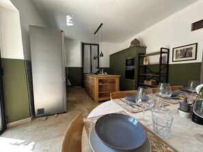 A dining area with a table set for two, a kitchen in the background, and a small dining table with glasses and plates.
