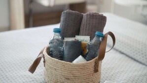 Una cesta tejida sobre una cama con una botella de agua, una toalla y un objeto pequeño.