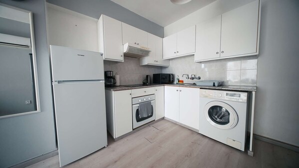 A modern kitchen with white cabinets, a built-in oven, a microwave, a coffee maker, and a washing machine.