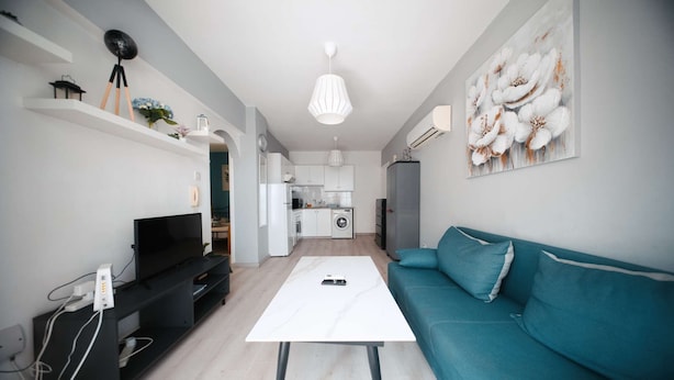 Un salon moderne comprenant un téléviseur, un canapé et une table basse, qui donne sur une cuisine et un coin repas.