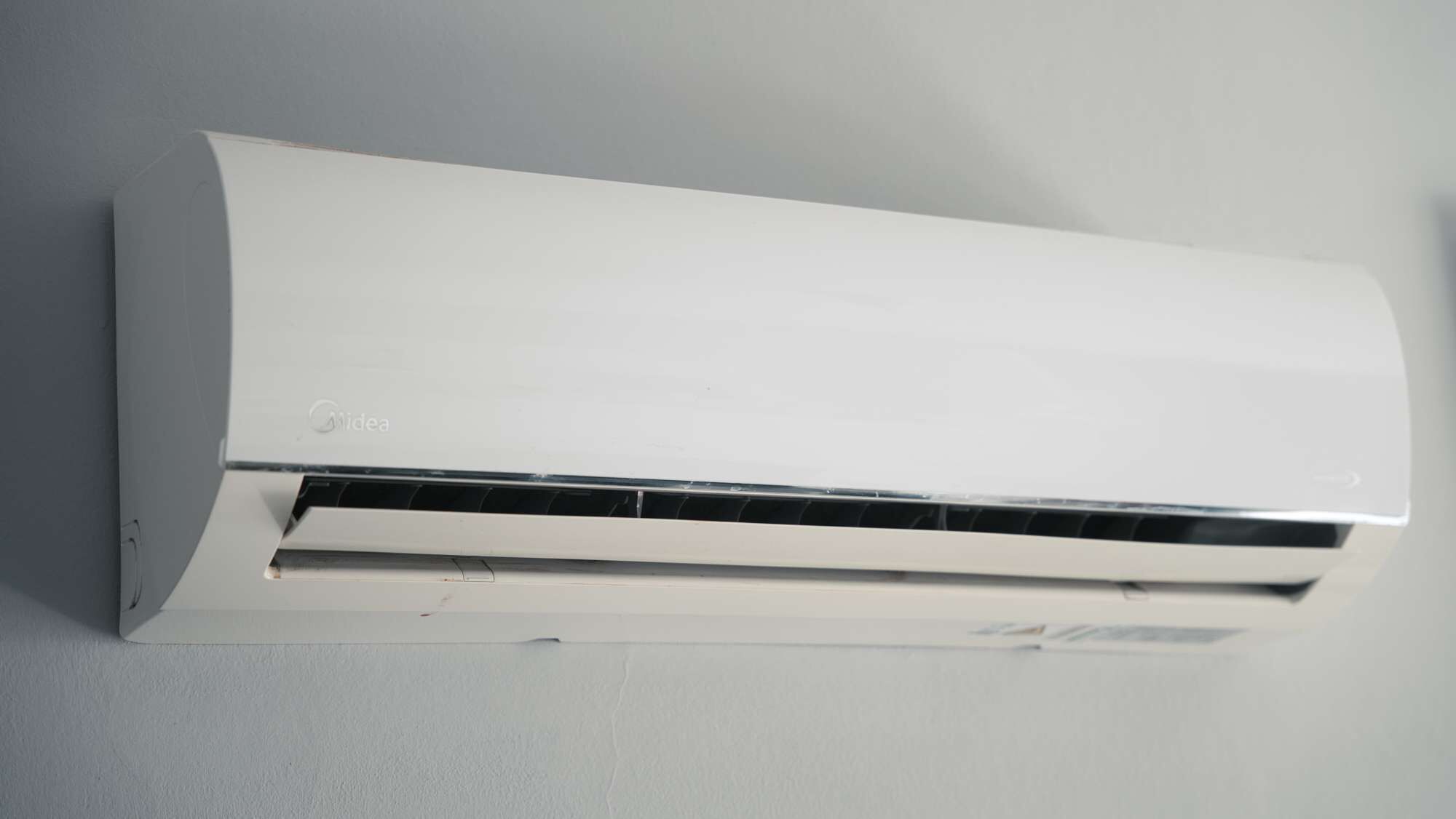 Un climatiseur mural blanc, doté d’un panneau de commande et d’une grille d’aération.