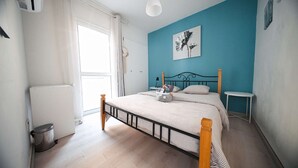 Une chambre à coucher avec un lit, des tables de chevet, un radiateur, une poubelle et une fenêtre.