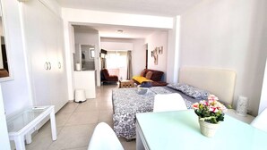 Ein kleines Hotelzimmer mit Bett, Tisch, Stuhl, Schreibtisch, Kleiderschrank, Bad und Küchenzeile.