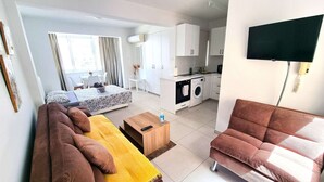 Ein modernes, helles Zimmer mit Bett, Sofa und einer kleinen Küchenzeile.