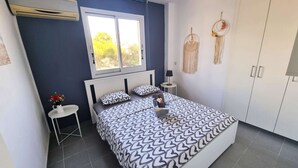 Een slaapkamer met een bed, een raam, een nachtkastje, een lamp en een kledingkast.