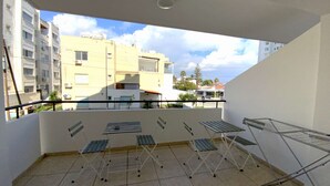 Un balcone con vista sugli edifici vicini, una stendibiancheria in metallo e un pavimento piastrellato.