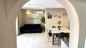 Un soggiorno con un divano nero, un tavolo da pranzo con sedie, una lampada a sospensione e una pianta in vaso.