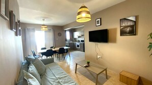 A living room with a sofa, a coffee table, and a TV mounted on the wall. - 2Br Apt - 5mins walk to the Beach + Netflix access (Larnaca)
