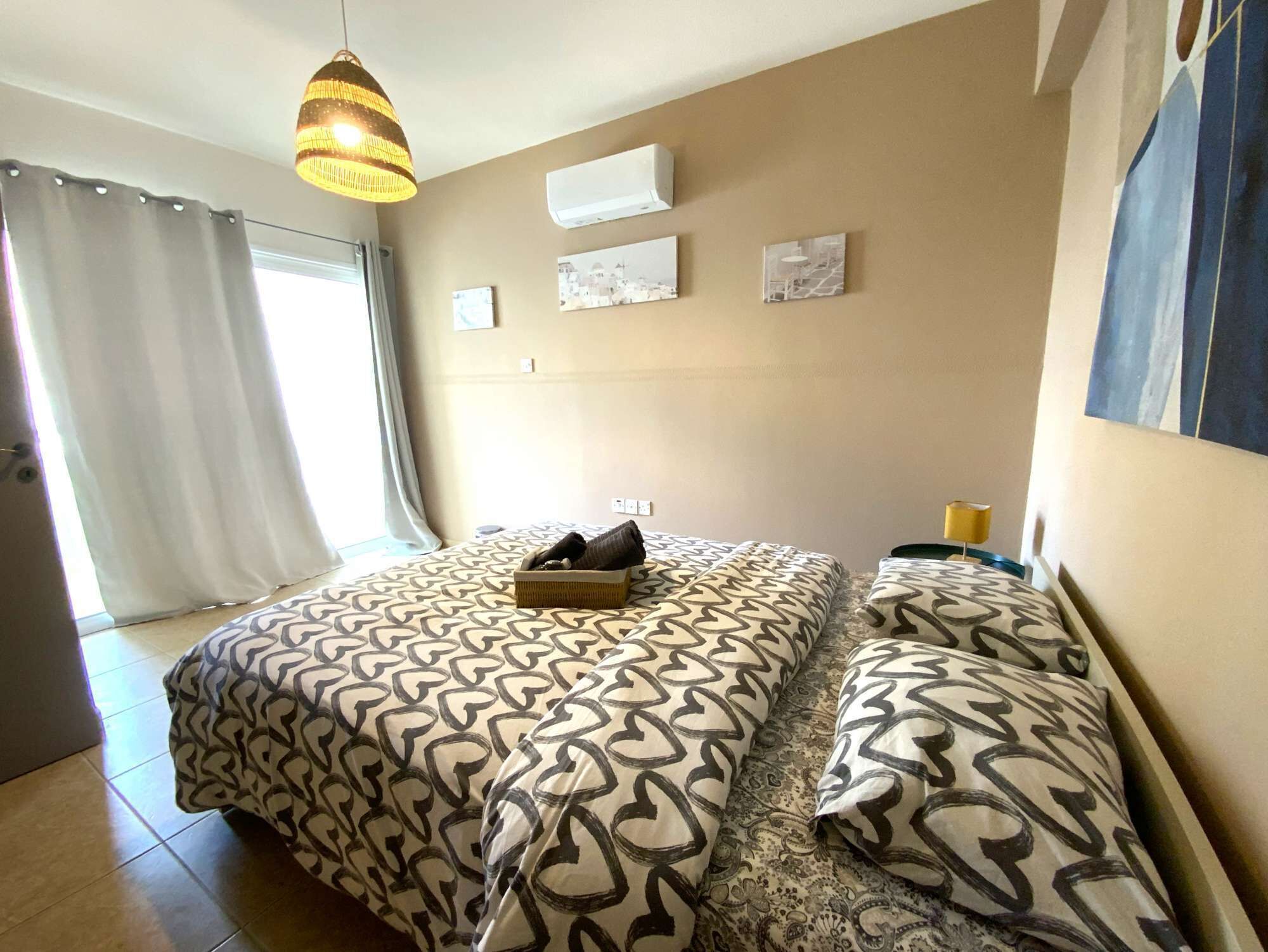 A bedroom with a bed, a hanging light fixture, an air conditioning unit, and a window with curtains.