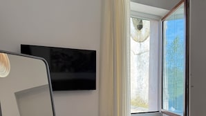 Ein modernes Hotelzimmer mit einem Bett, einem an der Wand montierten Fernseher, einem Fenster mit Vorhängen und einem Sessel.