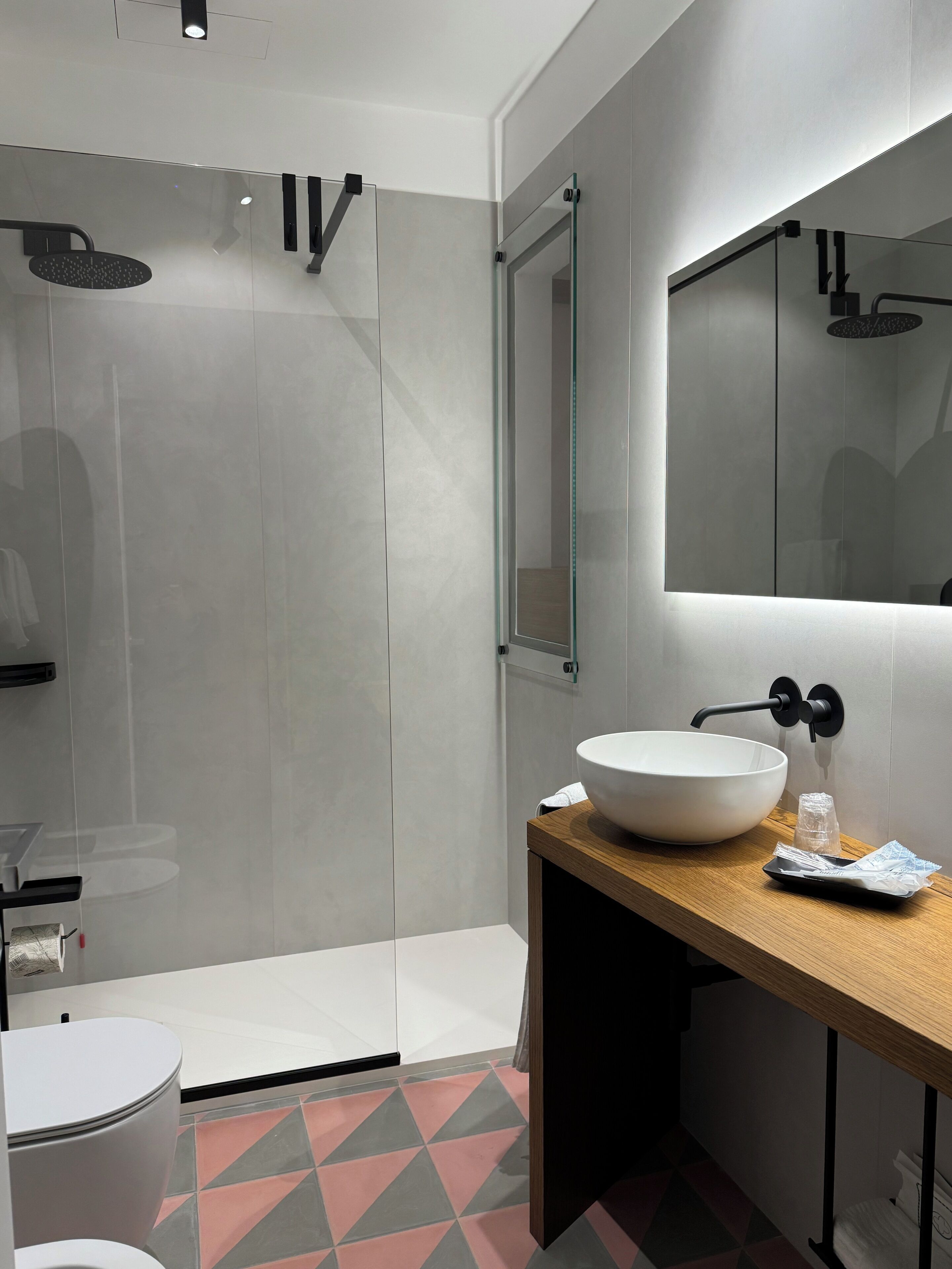 Une salle de bain moderne avec une douche à parois de verre, un lavabo blanc doté d’un grand bac et un miroir au-dessus du lavabo.