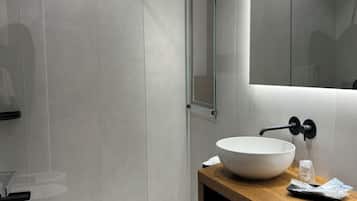 Une salle de bain moderne avec une douche à parois de verre, un lavabo blanc doté d’un grand bac et un miroir au-dessus du lavabo.