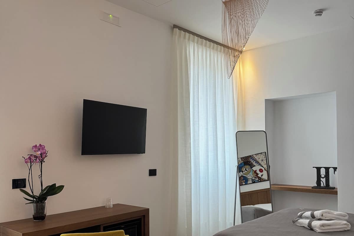 Une chambre d’hôtel moderne équipée d’un lit, d’un bureau avec une chaise, d’une télévision et d’un grand miroir.