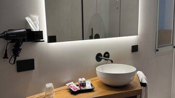 A modern bathroom with a large mirror, a wooden vanity, a white sink, and a towel hanging on the wall.
