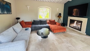 Una sala de estar con un sofá seccional, una mesa de centro de vidrio, una chimenea y un televisor montado en la pared.