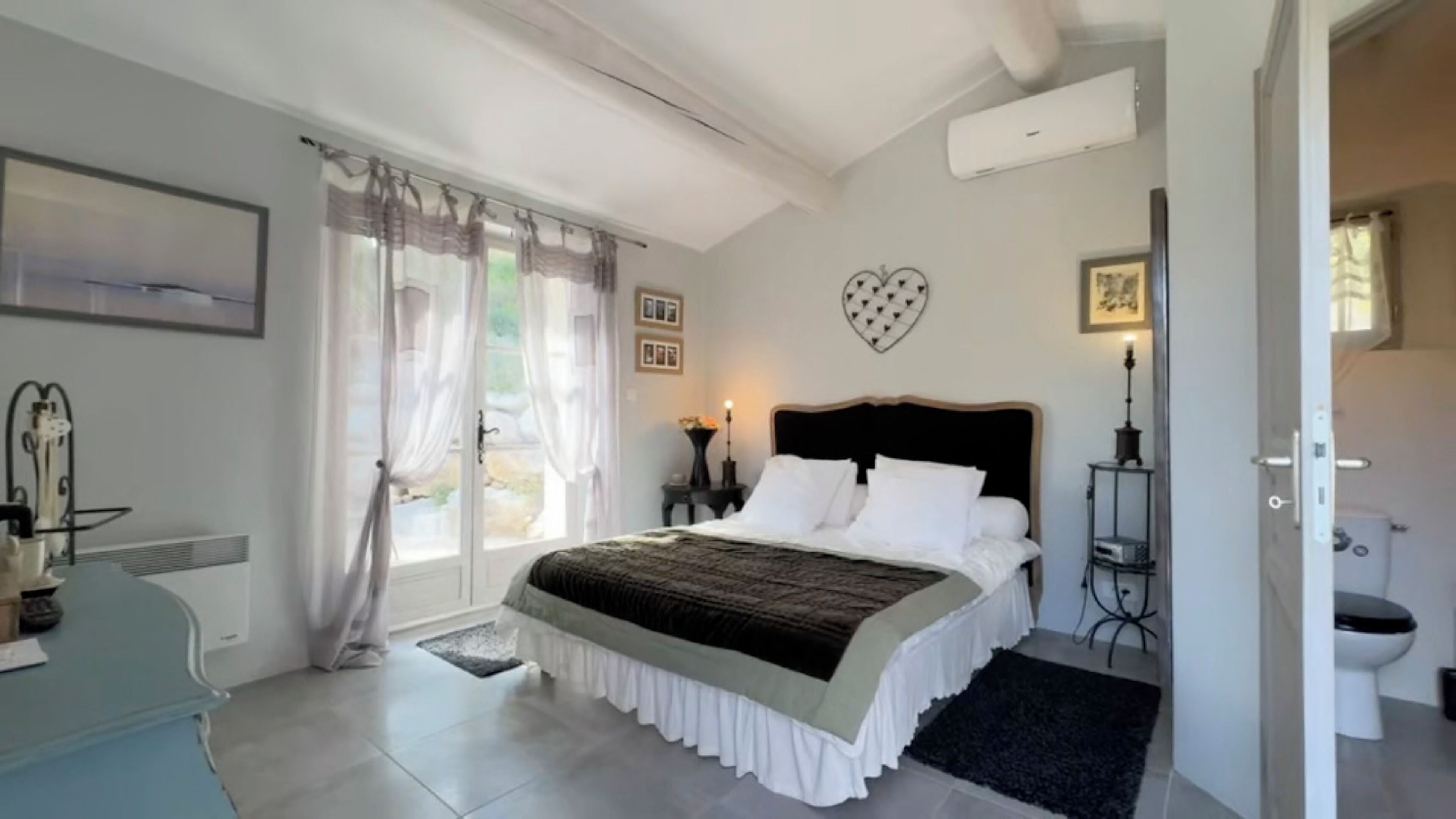 Une chambre à coucher comprenant un lit, un bureau, une chaise, une fenêtre avec des rideaux, une horloge murale et un objet décoratif en forme de cœur.