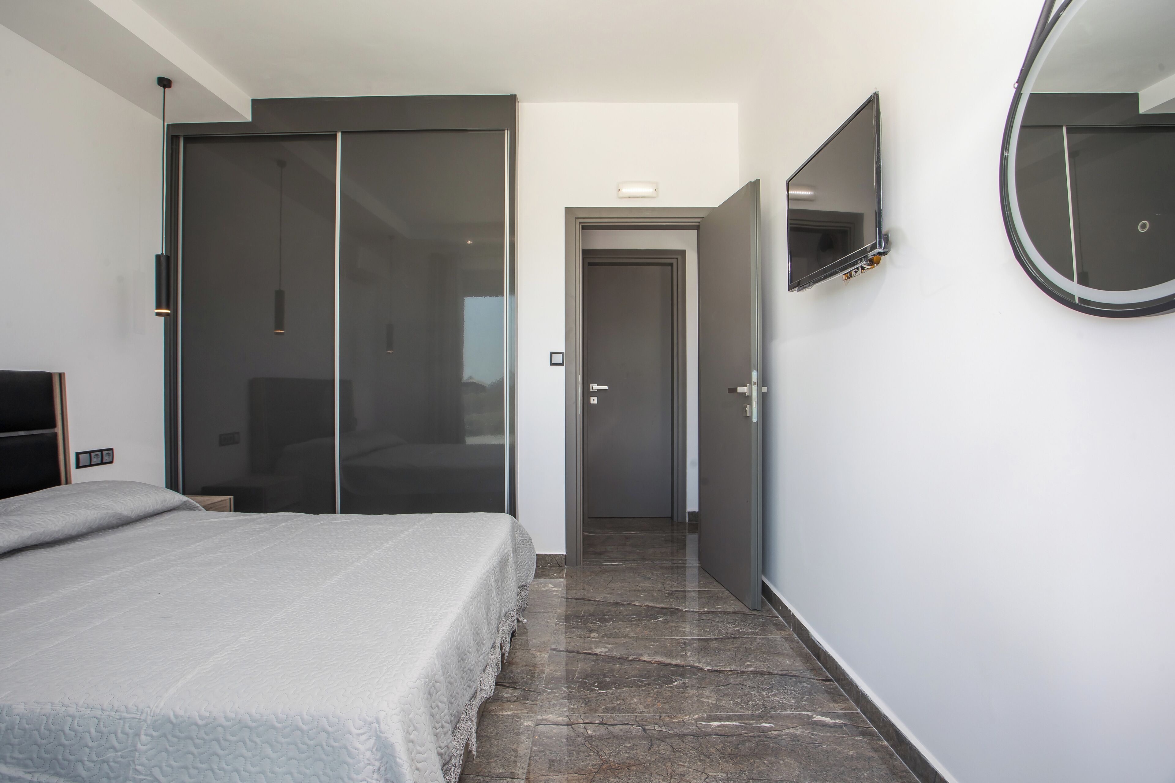 A modern hotel room with a large bed, a sliding door closet, a round mirror, and a small TV.