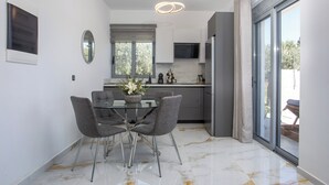 A modern kitchen with a glass dining table, grey chairs, and a marble floor. - Marinas villas (Rhodes)