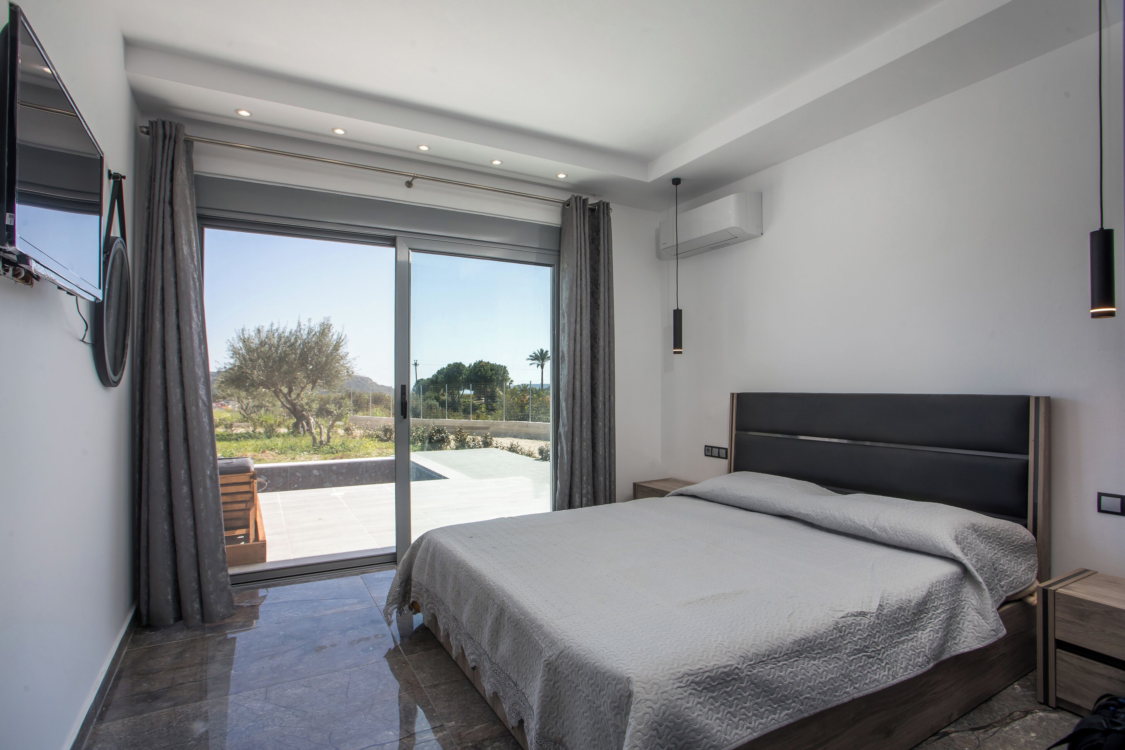Un dormitorio moderno con una cama grande, una puerta corrediza de vidrio que da a un balcón y un televisor de pantalla plana montado en la pared.