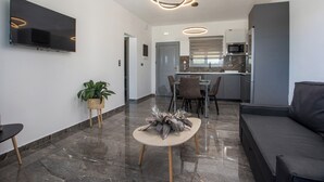 A modern living room with a flat-screen TV, a dining area with a table and chairs, and a kitchen with a microwave and refrigerator. - Marinas villas (Rhodes)