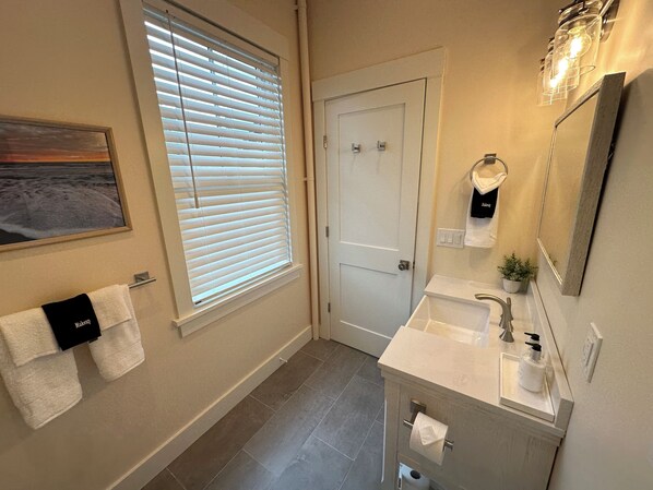 Un baño con un ventanal grande, un lavabo, un espejo y un perchero para toallas.