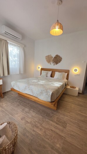 Ein Schlafzimmer mit einem hölzernen Bett, einer Pendelleuchte, einer Wand-Klimaanlage und einem fensterbepflanzten Fenster mit Vorhängen.