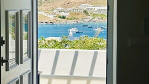A door leading to a balcony with a view of a coastal town and boats.
