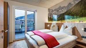 Een moderne slaapkamer met een groot bed, een schuifdeur naar een balkon en een muurschildering van een berglandschap.