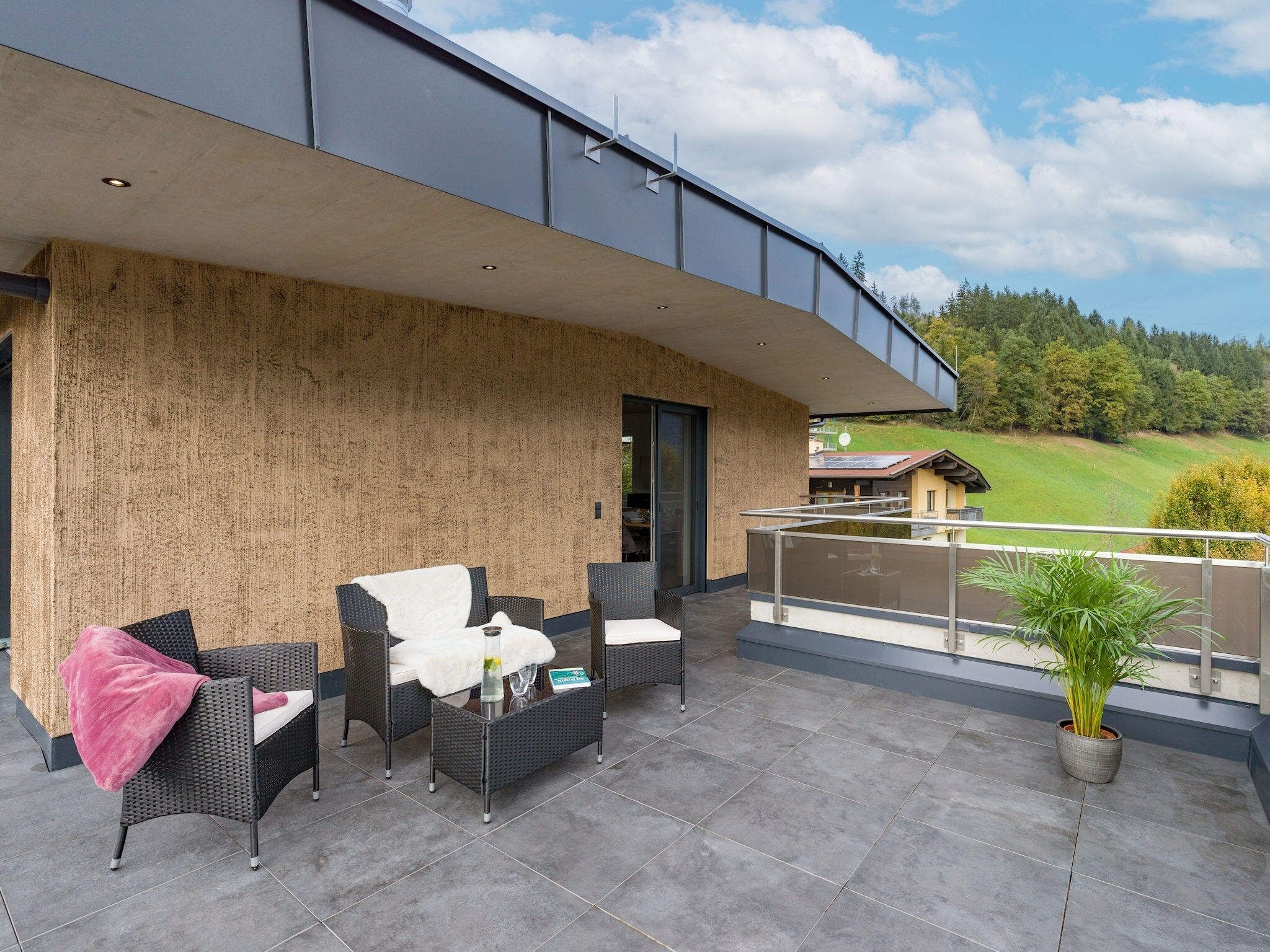 Eine moderne Terrassengestaltung mit Korbmöbeln, einem Blumentopf und Blick auf eine grüne Landschaft.
