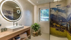 Een moderne badkamer met een grote spiegel, een wastafel, een douche met een bergfries en een raam met uitzicht op de omgeving.