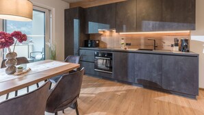 Una cocina moderna con armarios oscuros, una mesa de comedor de madera y un ventanal grande.