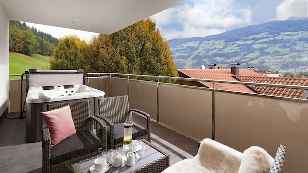 Un balcón con mobiliario de mimbre, una mesa dispuesta con té y tazas, y vistas a un paisaje montañoso.