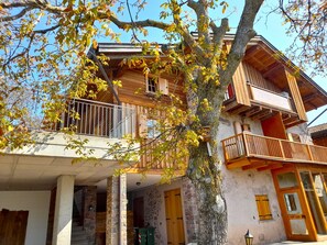 A wooden building with multiple balconies, a stone staircase, and a tree in the foreground.