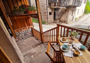 A wooden balcony with a table set for breakfast, including bread, coffee, and pastries.