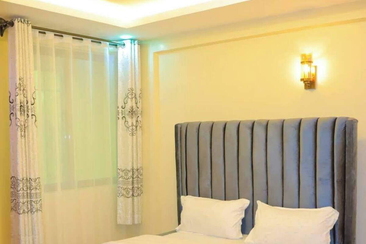 A neatly made bed with white linens and pillows, a padded headboard, and a wooden floor.