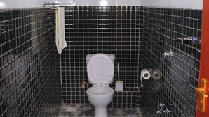 A small bathroom with a toilet, a shelf with toiletries, and a shower head. - Lux Suites Taris Apartments Rongo (Rongo)